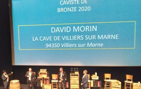 David Morin sur la scène de la remise de médailles, décoration rustique et bouteilles de vin.