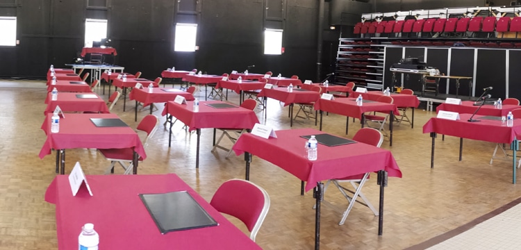 Grande salle avec tables, chaises et chevalets, prête à accueillir une réunion.