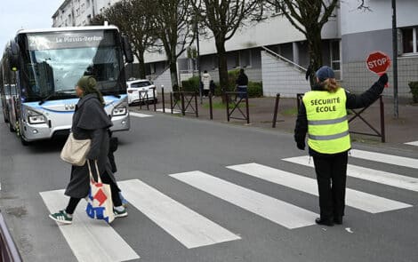 Un agent stoppe un bus et fait traverser une personne en toute sécurité sur un passage piéton.