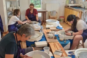 Des élèves du cours de poterie en apprentissage suivent les conseils de l'enseignante.