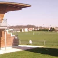 Terrain du complexe sportif, avec pelouse synthétique, à proximité de la tribune spectateurs.