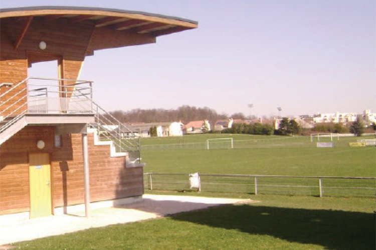 Terrain du complexe sportif, avec pelouse synthétique, à proximité de la tribune spectateurs.
