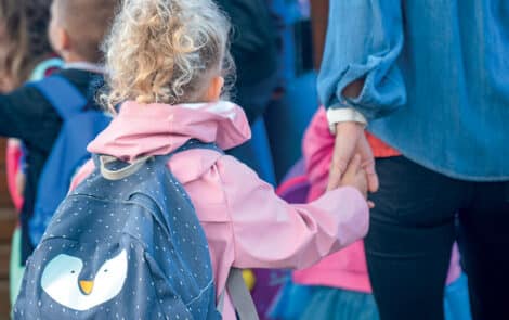 Une enfant, sac au dos, tenant un adulte par la main.